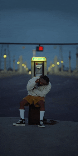 a man sits in front of a payphone that says telephone on it