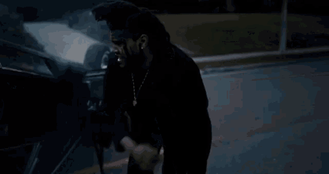 a man is standing in front of a car in the dark and screaming .