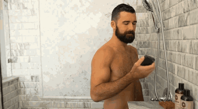 a shirtless man is taking a shower in a bathroom with bottles of shampoo on the shelf