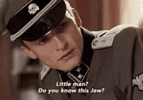 a man in a military uniform with a skull on his hat is talking to another man .