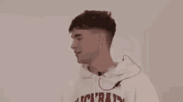 a young man wearing a white hoodie with a microphone around his neck is smiling .