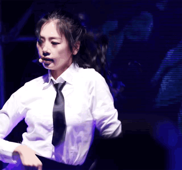a woman in a white shirt and black tie is dancing in front of a microphone