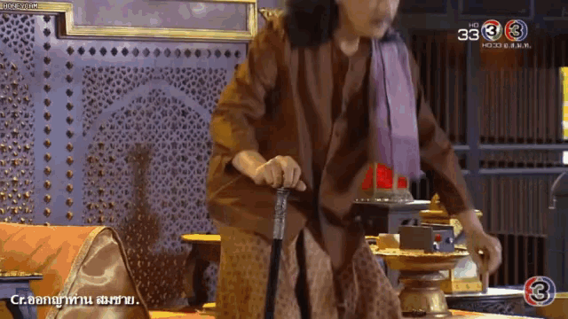 a man with long hair is holding a cane in front of a tv screen that says 33