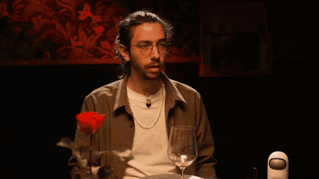 a man is sitting at a table with a glass of wine and a rose