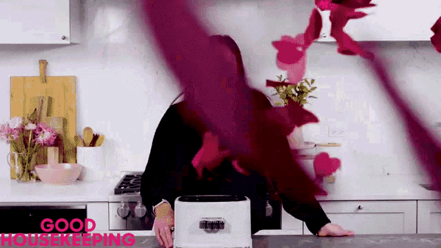 a woman is standing in a kitchen in front of a toaster with the words good housekeeping written on the bottom