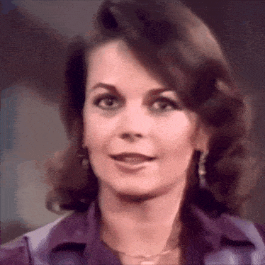 a close up of a woman 's face with a purple shirt and earrings