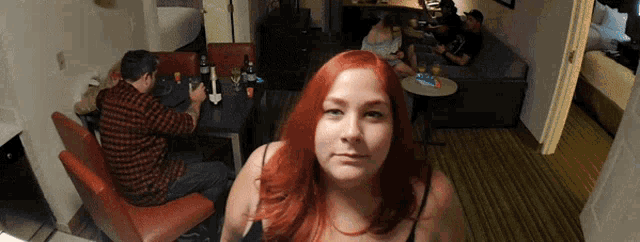 a woman with red hair stands in front of a group of people in a living room