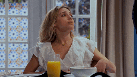a woman is sitting at a table with a glass of orange juice and a bowl of cereal