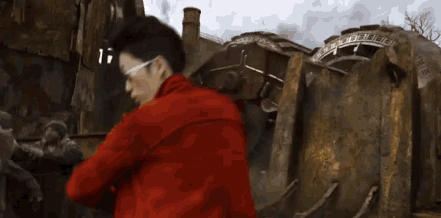 a man in a red jacket and sunglasses is holding a gun in front of a building .