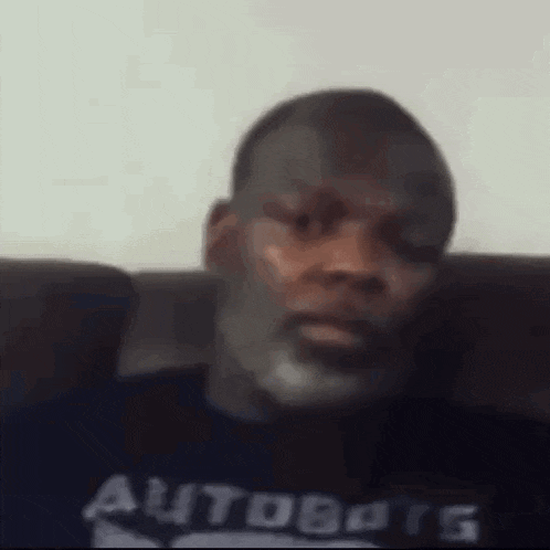 a man with a beard is sitting on a couch wearing a t-shirt that says autobots .