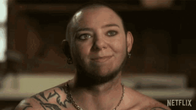 a man with a shaved head and a tattoo on his chest is smiling for the camera .