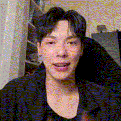 a young man in a black jacket is smiling and looking at the camera in a room .