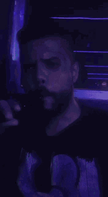 a man with a beard is standing in a dark room with purple lights behind him