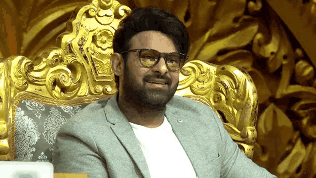 a man wearing glasses and a suit is sitting in a gold chair