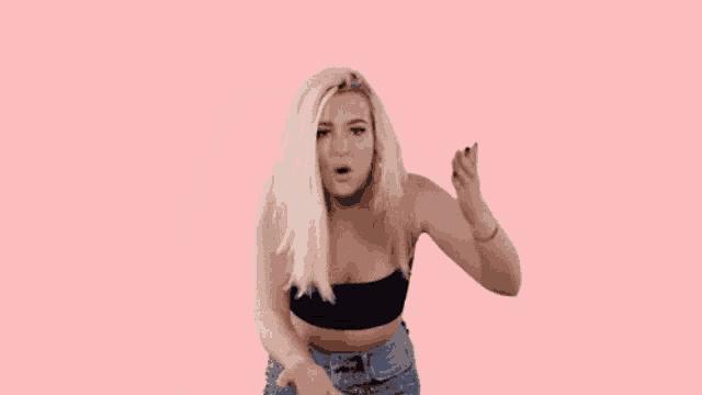 a blonde woman is standing in front of the word wtf on a pink background .