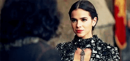 a woman in a black dress and necklace is standing next to a man in a castle .