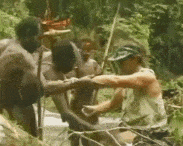 a group of people are standing around a man in a jungle .