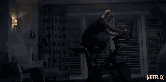 a woman riding an exercise bike in a dark room with a netflix logo on the bottom