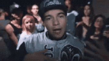 a man in a baseball cap is standing in front of a crowd of people in a club .