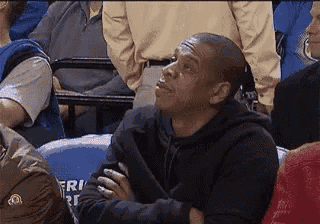 a man in a black hoodie is sitting in a crowd of people watching a game .