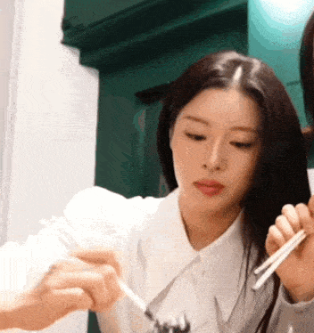 a woman in a white shirt is holding chopsticks