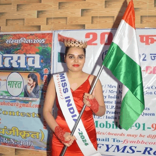 a woman in a red dress is holding a flag and wearing a miss india sash