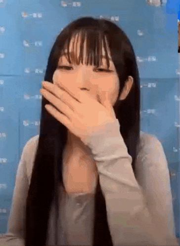 a young woman is covering her mouth with her hand .