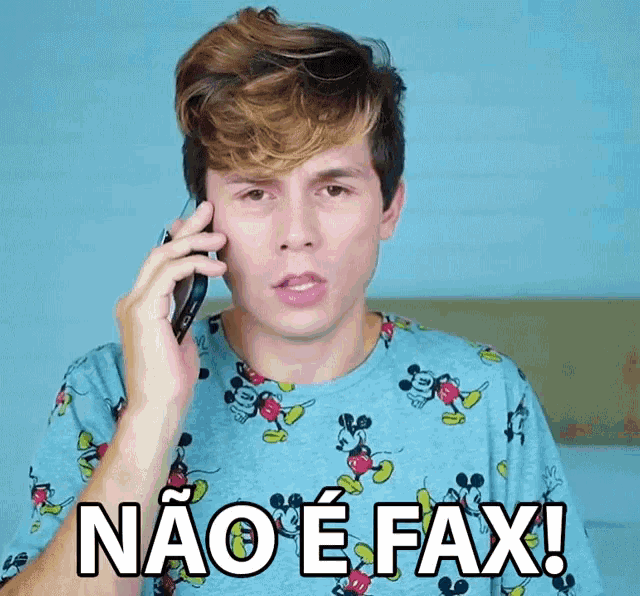 a man wearing a mickey mouse shirt is talking on a cell phone and says " nao e fax "
