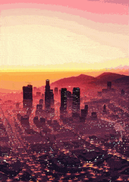 an aerial view of a city with mountains in the background at sunset