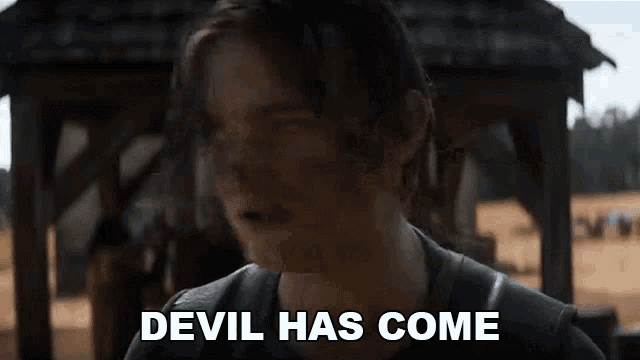 a man in a black shirt is standing in front of a wooden structure and says `` devil has come '' .