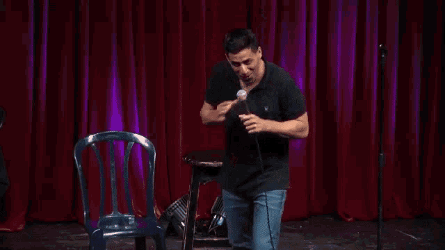 a man in a black shirt is standing in front of a red curtain holding a microphone .