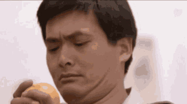 a man is holding an orange in his hand and making a face .