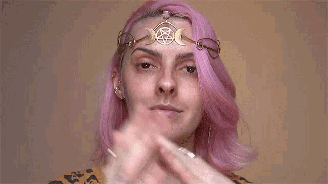 a woman with pink hair is wearing a gold crown on her head .