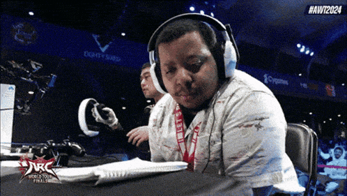 a man wearing headphones is sitting at a table with a sign that says # awt2024