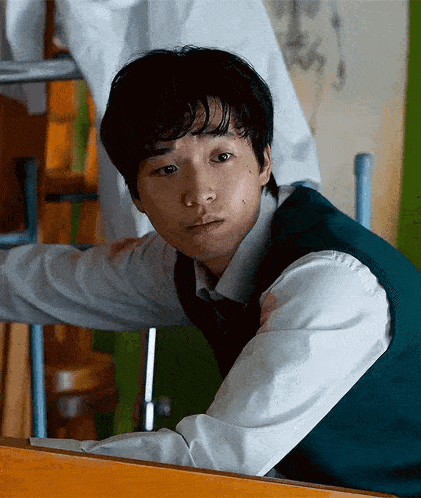 a young man wearing a green vest and white shirt