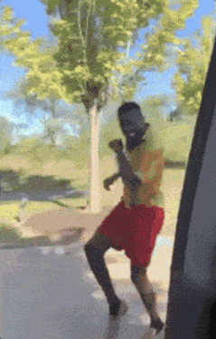 a man in red shorts and a yellow shirt is dancing in front of a tree