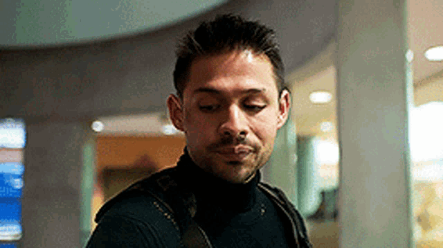 a man wearing a black turtleneck and a backpack looks down