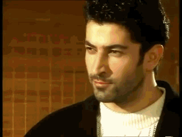 a man with a beard wearing a black jacket and white sweater