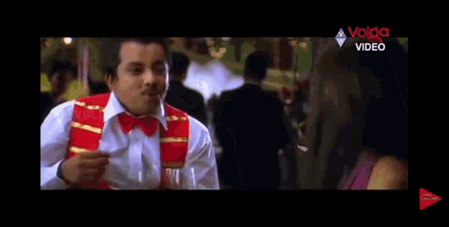 a man in a red vest and bow tie is talking to a woman in a movie .