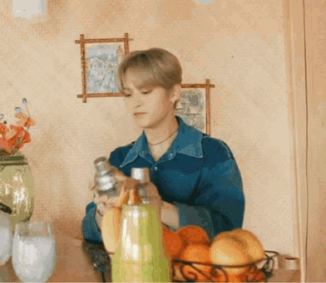 a man in a blue shirt is holding a shaker in front of a basket of fruit .