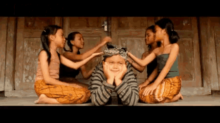 a group of young girls are sitting around a young boy with a crown on his head