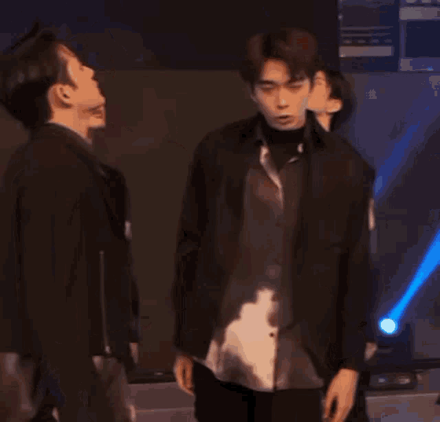 a group of young men are standing next to each other on a stage and one of them is pointing at the other .