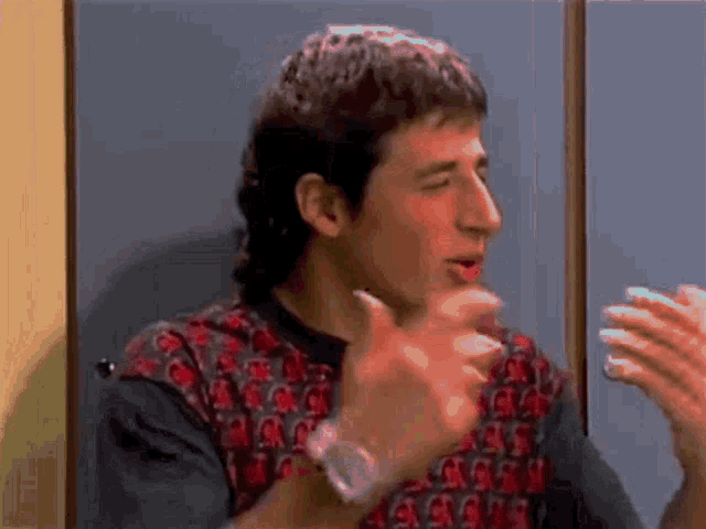 a man wearing a watch and a mullet is talking to another man