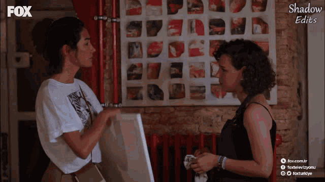 two women are talking in front of a wall that says shadow edits