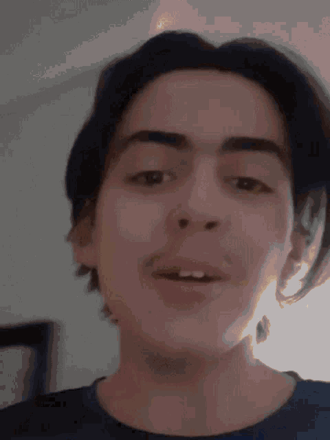a young man with long hair and a beard is making a funny face while wearing a blue shirt .