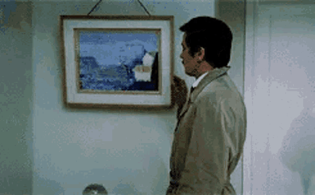 a man in a trench coat is looking at a framed picture on a wall .