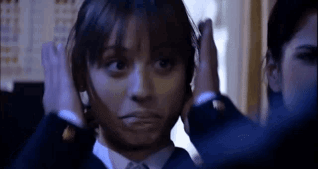 a woman in a suit and tie has her hands on her head .