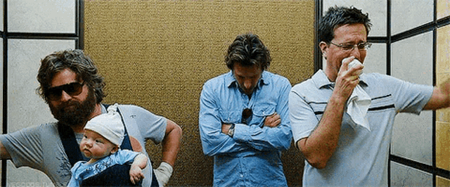 a man with a beard is holding a baby while another man wipes his nose with a napkin