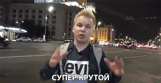 a man wearing a shirt that says levi is standing on a city street