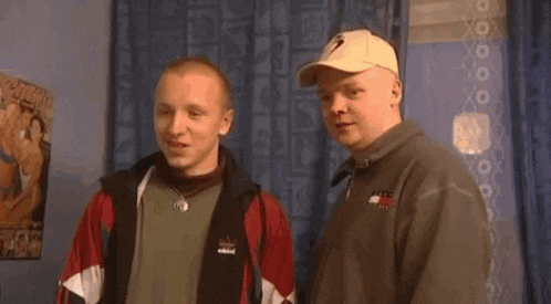 two men are standing next to each other in a room and talking to each other .